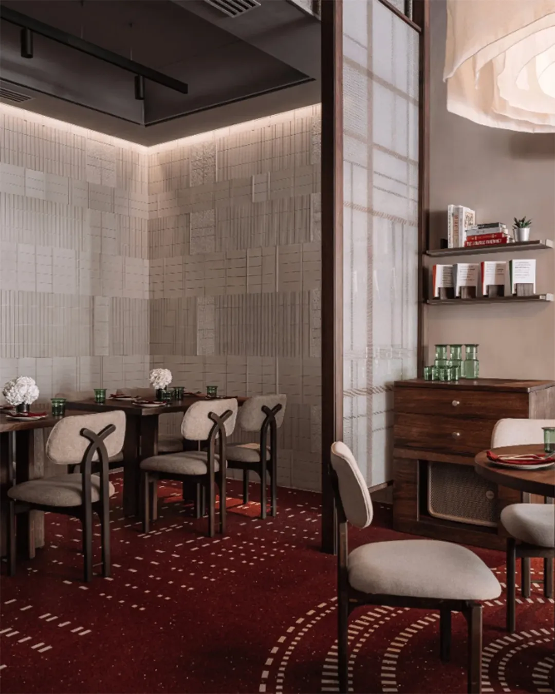 Elegant restaurant corner with textured beige wall tiles, modern wooden tables, curved-back upholstered chairs, and deep red patterned flooring creating a warm, contemporary dining atmosphere.