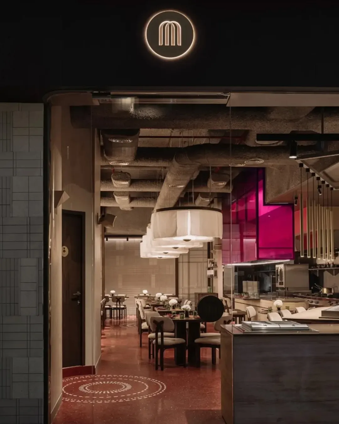 Modern upscale restaurant entrance with a minimalist circular logo illuminated above. The interior features stylish lighting and a clean, elegant design.