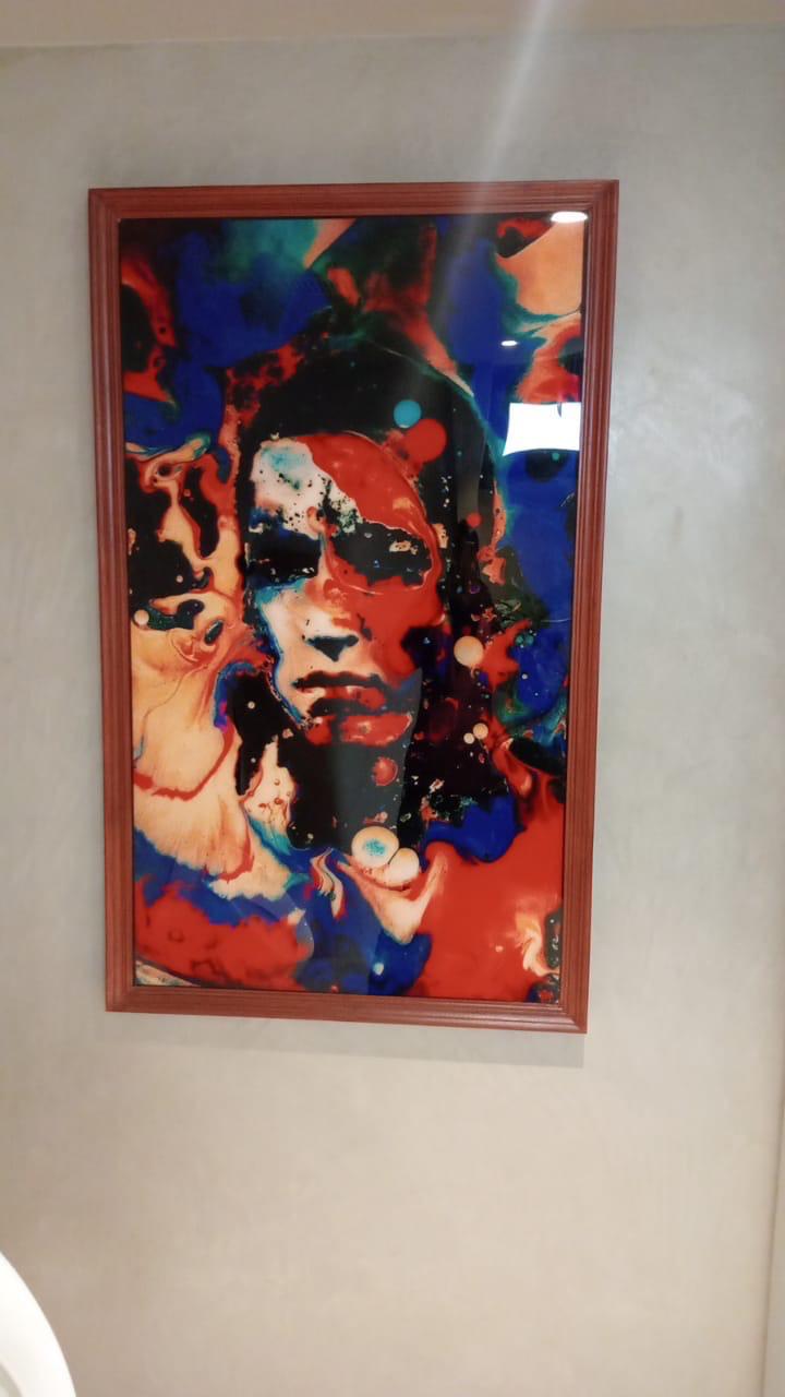 Abstract colorful painting with a vibrant face design in red, blue, and orange tones, framed in wood, creating a striking visual effect in a modern interior.
