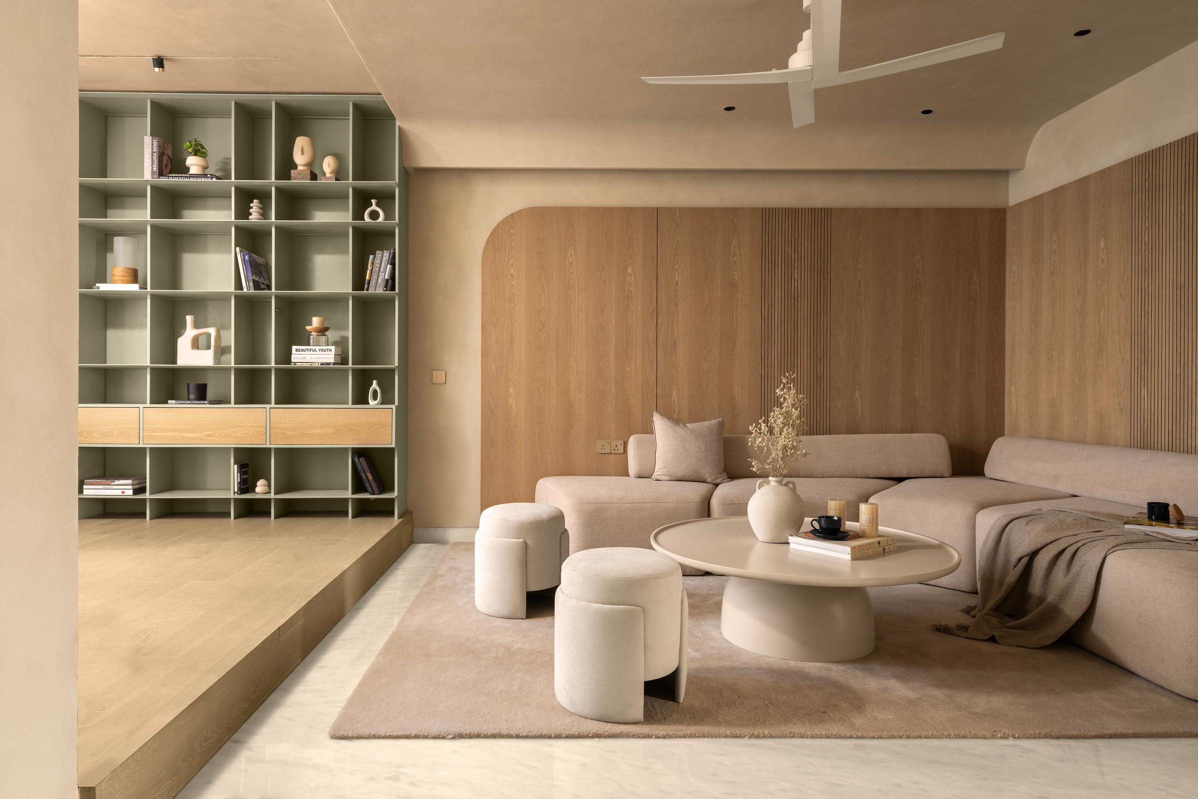 Stylish living room with modern minimalist design featuring a light beige sectional sofa, a round coffee table, and soft, plush ottomans. The room is highlighted by a green open shelving unit with decorative objects and books.