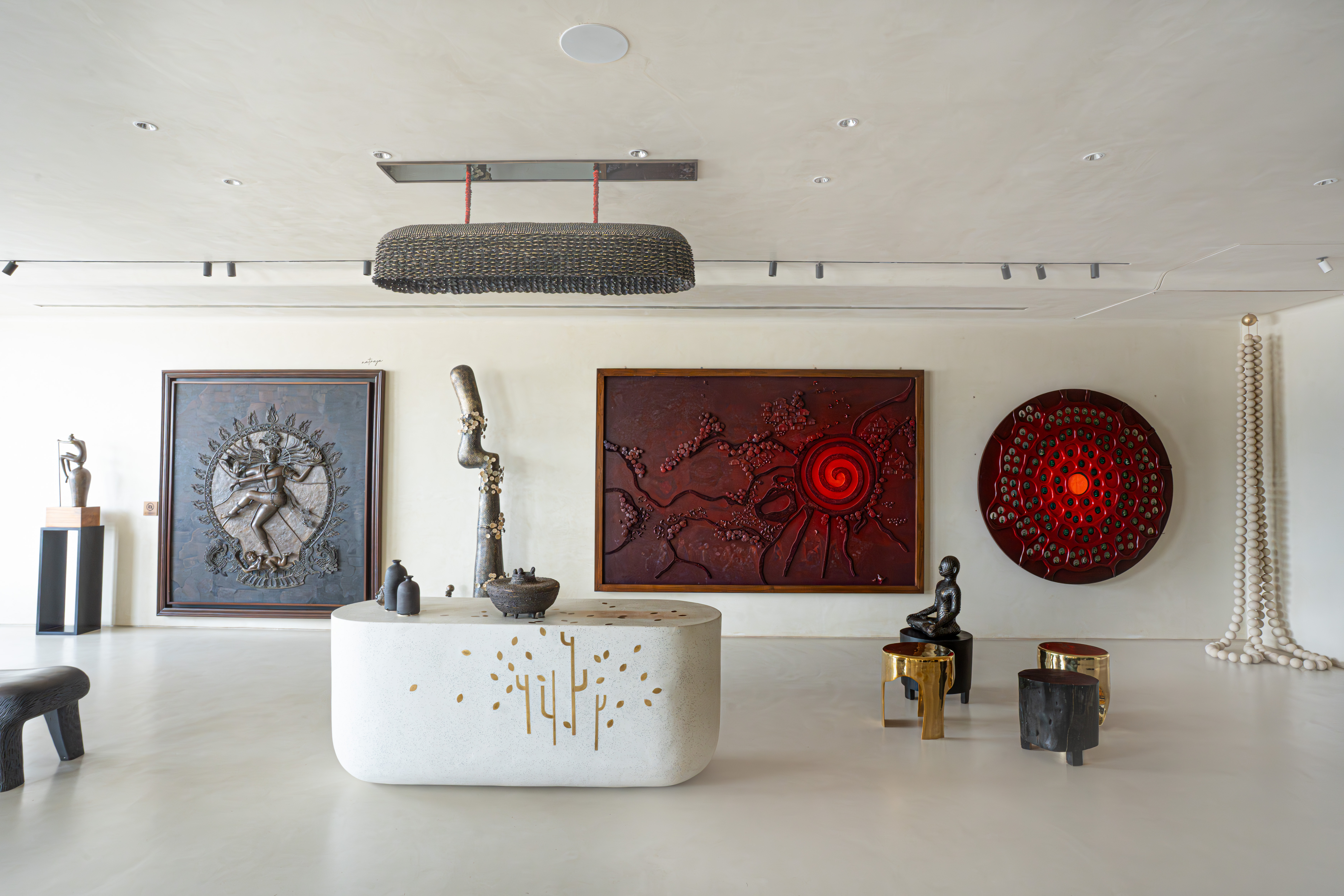 Minimalist contemporary gallery — white stone reception island with gold inlay, bronze abstract floor sculpture, and a large red spiral relief panel.