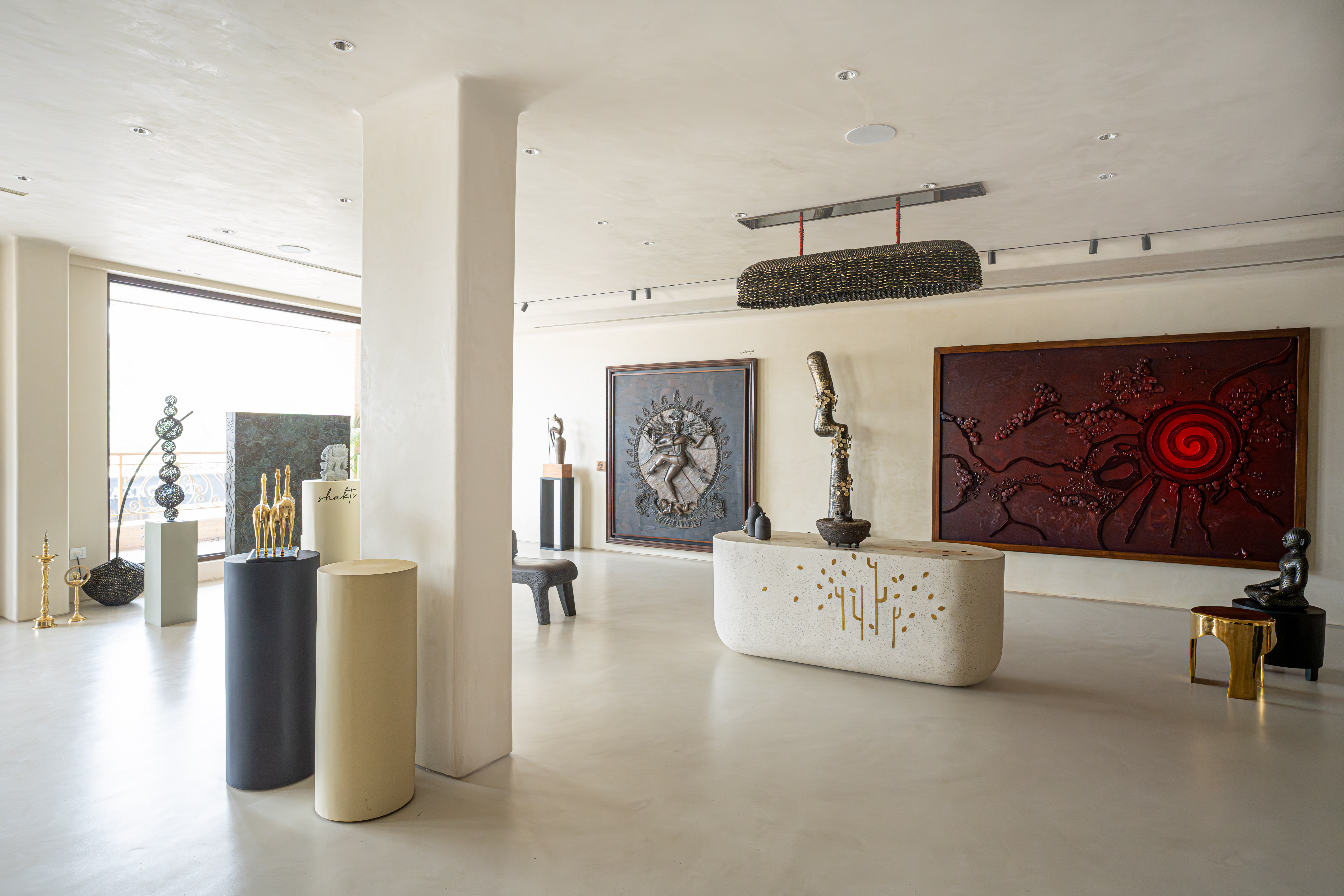 Minimalist contemporary art gallery interior with sculptures on pedestals, a stone reception desk with gold inlay, and a large red spiral relief painting.